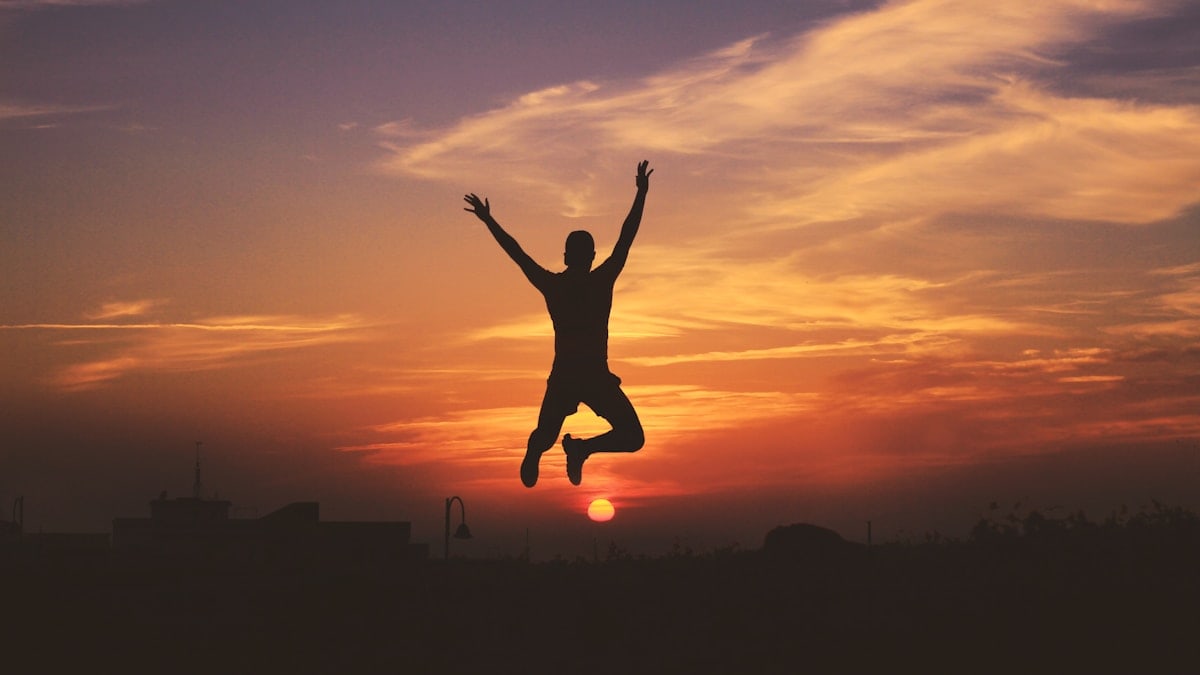 silhouette of man jumping raising both hands during golden hour